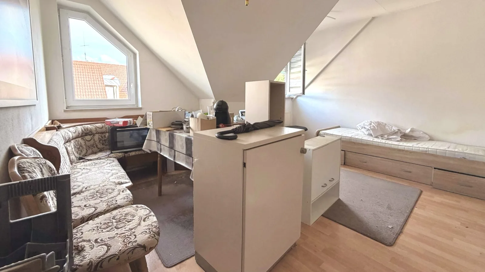 Dieselbe Dachgeschosswohnung in Weiden vor der Entrümpelung: Sofa, Schränke, Bett und Hausrat im Raum
